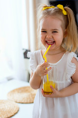 Little girl drinks fresh orange juice from a glass cup in the kitchen © Марина Гаращенко