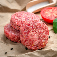 Homemade raw ground beef and Burger Patty with Basil, tomatoes and seasonings on craft paper.