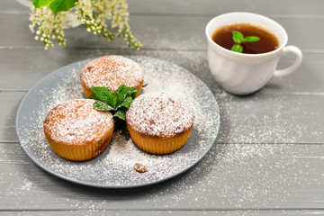 Composition with a cup of tea, cupcakes and white cherry flowers on a wooden background.