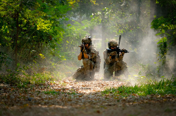 Two soldiers with the fighting uniform sit on the ground and point gun to target for the concept...