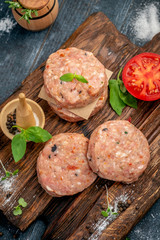 Homemade raw ground beef and Burger Patty with Basil, tomatoes and seasonings on a wooden Board.