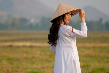 Vietnamese girl stand and turn back in the field with evening light with forest and mountain as background.
