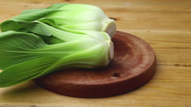 Male hand puts fresh green bok choy or pac choi chinese cabbage on a brown wooden kitchen board. Side view, close up.