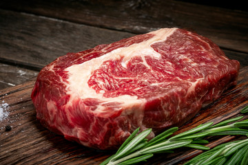 Raw rib eye steak of beef on wooden Board with rosemary and thyme on wooden background