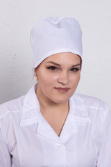 Portrait of attractive young female doctor in white medical jacket and  white medical cap on a grey background.