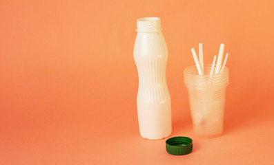 plastic dishes. Bottle and glass with spoons on a pink background. Plastic recycling concept....