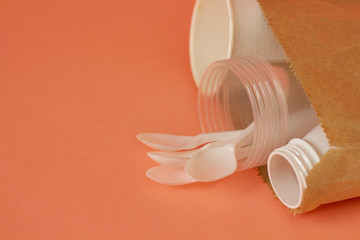 plastic dishes. Disposable plastic bottle, glasses in a paper bag. On a pink background. Plastic recycling concept. Ecology. copyspace
