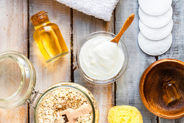 Concept of natural organic ingredients in cosmetology and gentle home treatment in quarantine. Do it yourselft. Handmade mask with oat, yogurt, oil. Wooden background. Flat lay top view close up
