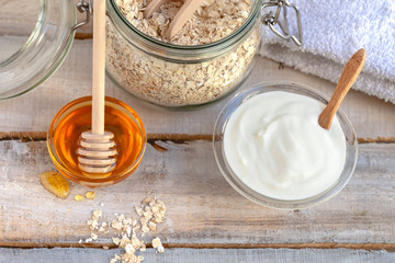 Concept of natural organic ingredients in cosmetology and gentle home treatment in quarantine. Do it yourselft. Handmade mask with oat, honey, yogurt for young skin. Wooden background. Close up macro