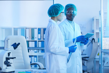 Two scientists in white coats discussing scientific experiment together while working at the laboratory