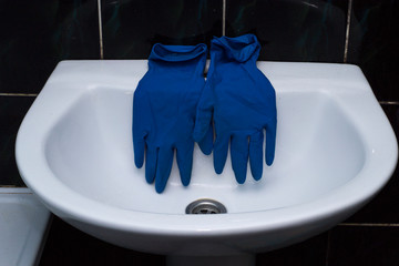 Blue rubber gloves on the sink. Bathroom cleaning.