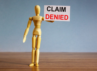 Wooden model of a man holding a tablet saying claim denied.