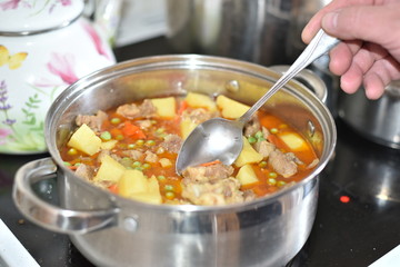In a saucepan, cooked stew vegetables: potatoes, carrots, peas with meat. The cook takes a sample with a spoon. Healthy food that is good for the stomach.