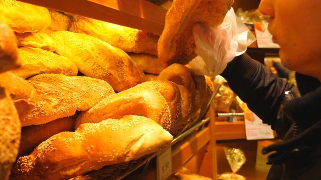Close up hand of male consumer taking fresh bread from baking shelf and smelling it. Man selecting flour products at supermarket. Buyer selecting goods. Concept of shopping. Slow motion