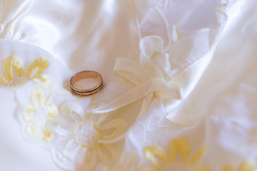 Vintage gold wedding band resting on cream and yellow satin embroidered old-fashioned slip in soft focus