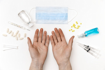 Man hands against the white background of pills, medical thermometer, mask, sterilization gel, ear sticks.  COVID-19, ncov flat lay composition, coronavirus prevention