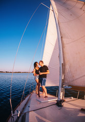 Happy couple in love on sailboat kissing when standing under sail on yacht