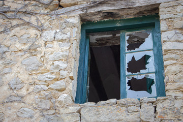 Wooden window with broken glass in old brick house. Abandoned medieval building with destroyed window. Damaged window in ancient stone wall. Vandalism and burglary concept. Antique architecture. 