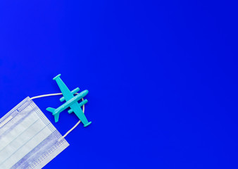 Airplane and medical face mask on a blue background. Flat lay, copy space, top view. Summer concept, pandemic, coronavirus.