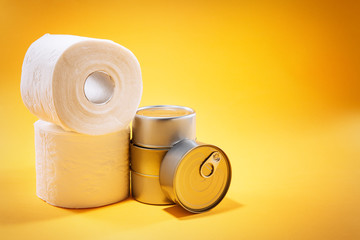 Toilet paper rolls next to canned goods, on top of yellow background, with available copy space. 