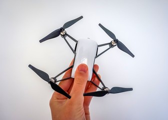 A mini small little white toy drone with a camera on a white background held in hand by a child or...