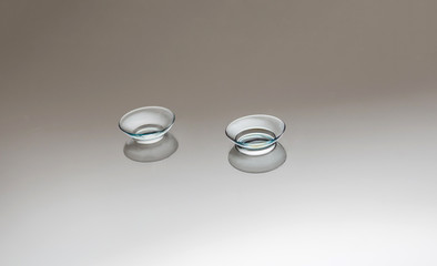 Transparent lenses on a gray background. Two pairs of clear lenses on a mirrored background with free space. Myopia, vision problems.