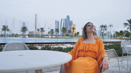 A girl in an orange dress sits at a table against the background of the evening Abu Dhabi.