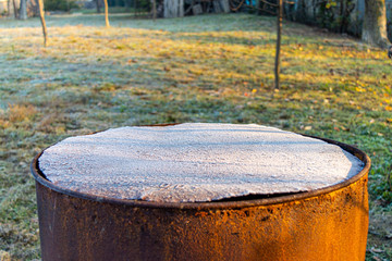 Iron rusty barrel covered by frost in garden