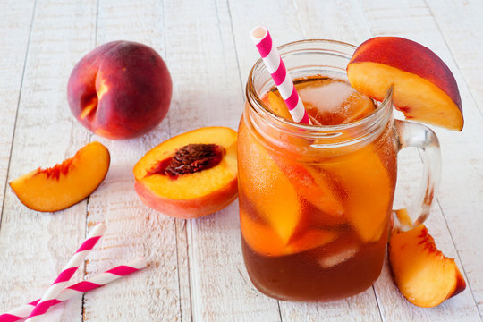 Homemade peach iced tea in a mason jar glass. Table scene with a white wood background.