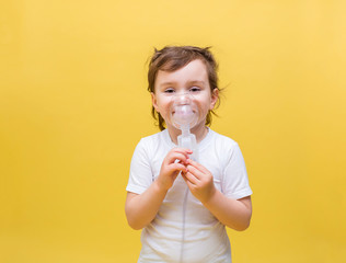 Cute little girl in a white t-shirt on a yellow background. A little girl is breathing through a mask. Diseases of the upper respiratory tract. Inhalations.