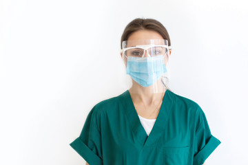 Portrait of a nurse girl on a white background in a green dressing gown, a protective mask and glasses. Woman look at the camera.. Copy space.