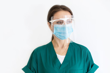 Portrait of a nurse girl on a white background in a green dressing gown, a protective mask and glasses. Woman look to the side. Copy space.
