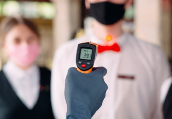 The Manager of a restaurant or hotel checks the body temperature of the staff with a thermal imaging device.