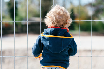Kind ausgegrenzt vor geschlossenerem Spielplatz stehend vor dem Zaun