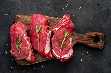 raw three beef steaks on a cutting board with spices on a stone background