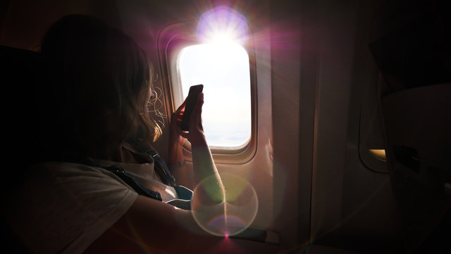 A girl takes pictures of beautiful landscapes from the airplane window using her phone.