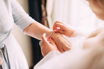 A bride puts a bracelet on her mom's arms close-up at her wedding, morning gatherings - obrazy, fototapety, plakaty