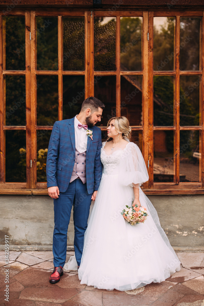 Wall mural Portrait of a wedding couple of the bride and groom in a beautiful suit and dress, floral bouquet in an incredible place, vertical photo