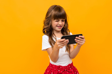 Beautiful little girl in dress play phone games isolated on yellow or orange background