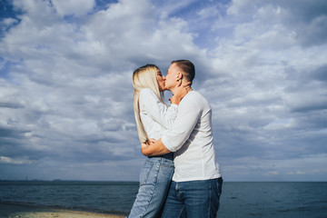 Charming young woman embracing with boyfriend on sea background. Outdoor photo of happy couple standing near ocean. Summer vacation concept. Casual style. Happy together. Outdoor shot