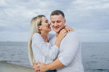 Charming young woman embracing with boyfriend on sea background. Outdoor photo of happy couple standing near ocean. Summer vacation concept. Casual style. Happy together. Outdoor shot