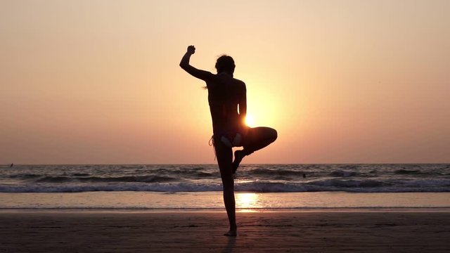 Silhouette of a woman who practices yoga on a sunset background at the beach