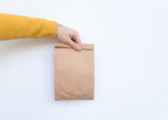 Male hand in a yellow sweater hold in hand brown clear empty blank craft paper bag for give takeaway isolated on white background. Packaging template mock up. Delivery service concept. Copy space