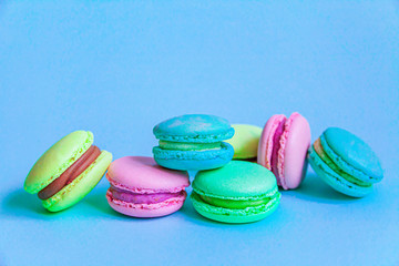 Sweet almond colorful pink blue yellow green macaron or macaroon dessert cake isolated on trendy blue pastel background. French sweet cookie. Minimal food bakery concept. Flat lay top view copy space.