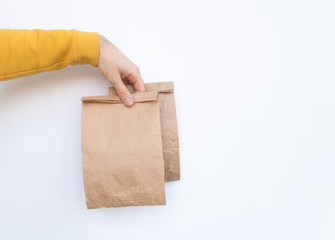 Fototapeta na wymiar Male in a yellow sweater hold in hand several brown clear empty blank craft paper bags for give takeaway isolated on white background. Copy space. Advertising area
