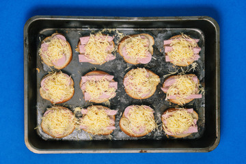 Sandwiches with sausage and cheese in a baking tray in the oven. The process of preparing a quick meal.