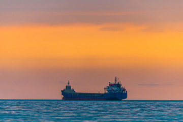 Obraz premium Cargo ship sailing the sea at a golden sunset or sunrise. Ocean shipment across water as the sun sets or rises. Harmony and beauty in nature. Scenic peaceful sea view