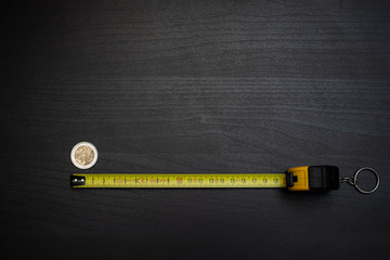 measuring tape measuring a coin on dark wooden table