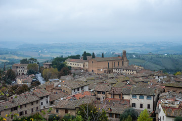Naklejka premium Famous place in Tuscany Italy.Medieval architecture of italian city.Panoramic view of rooftop cityscape and foggy landscape in background.Rainy autumn day in San Gimignano.Popular tourist destination