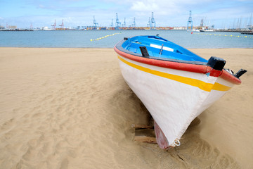 A simple wooden colorful fishing boat on the beach in the harbor.